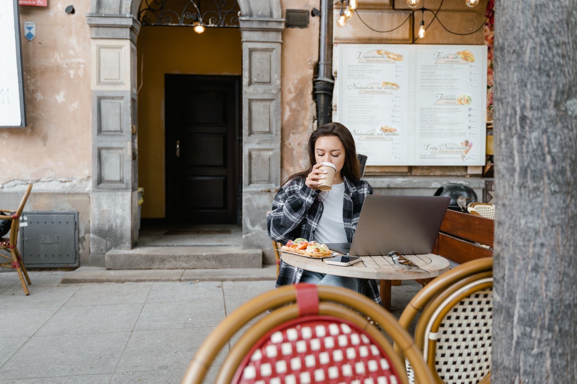 A woman relaxing with coffee at an outdoor café terrace, laptop open beside her.